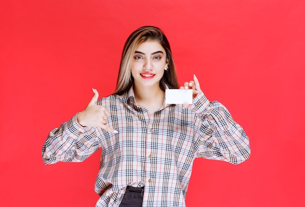 Fille en chemise à carreaux tenant une carte de visite et demandant un appel