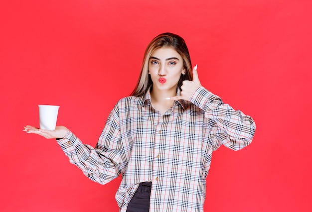 Fille en chemise à carreaux tenant une tasse de café jetable blanche et demandant un appel