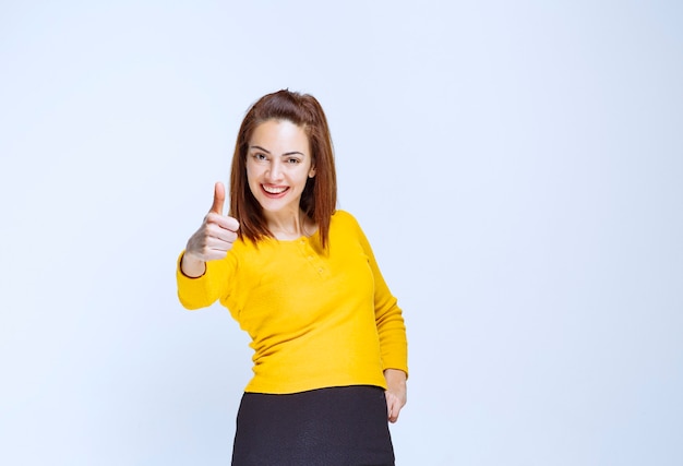 Fille en chemise jaune debout sur un mur bleu et se sentant positive.