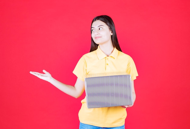 Fille en chemise jaune tenant une boîte cadeau en argent