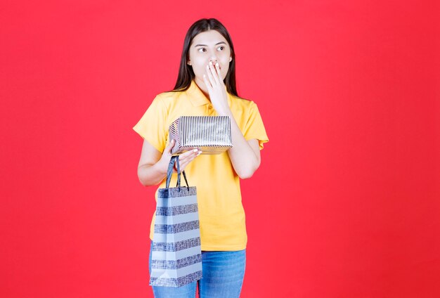 Fille en chemise jaune tenant un sac à provisions et une boîte-cadeau en argent et a l'air effrayée et terrifiée