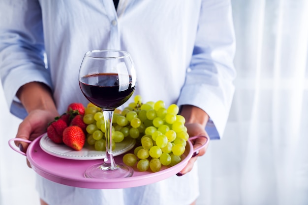 Fille en chemise tient un plateau de fruits et de vin sur fond blanc