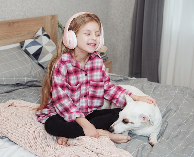 Fille et chien assis sur un canapé dans des écouteurs, écoutant de la musique avec son smartphone.