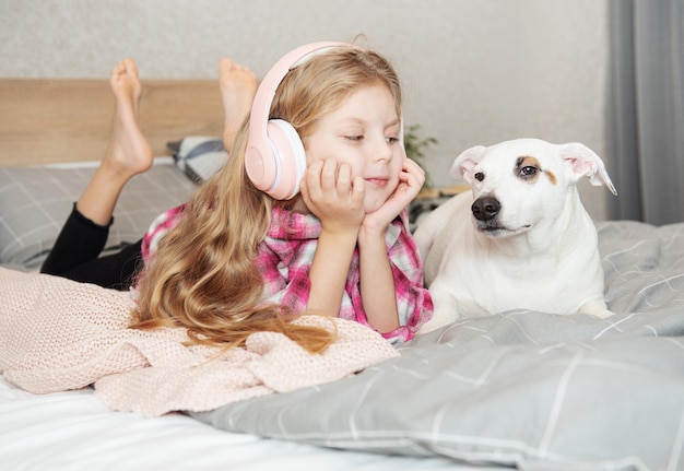 Fille et chien assis sur un canapé dans des écouteurs, écoutant de la musique avec son smartphone.