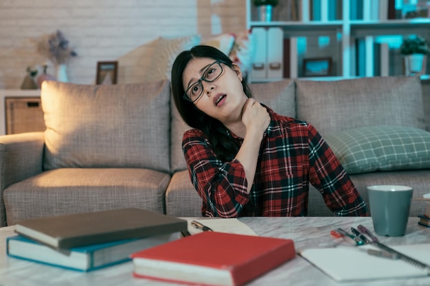 Photo la fille chinoise pleurniche en essayant de revivre la tension de l'épaule d'étudier sans relâche. une mauvaise posture assise cause des douleurs au cou à la jeune femme asiatique. concept de soins de santé et médical