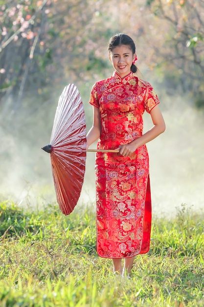 Fille chinoise avec une robe traditionnelle Cheongsam dans le jardin