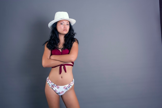 Fille chinoise sérieuse en bikini sur fond neutre, les bras croisés de mécontentement ou de colère