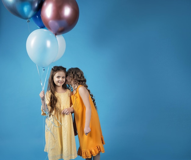 Une fille chuchote quelque chose à l'oreille d'une autre fille avec des ballons, une place pour le texte