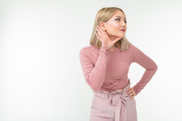 Fille avec une coiffure blonde tient la main à l'oreille conversation d'écoute sur blanc avec copie espace