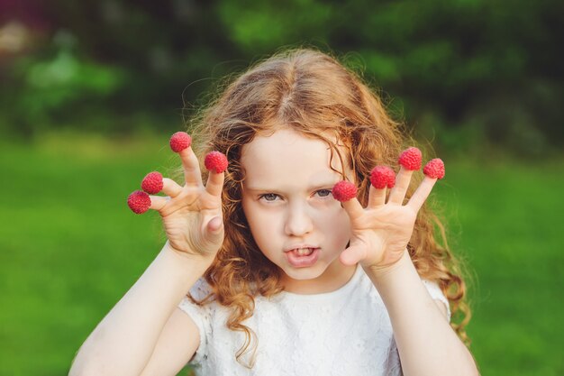 Fille en colère avec des framboises aux doigts.