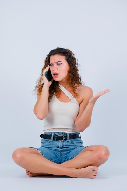 Fille en colère parle au téléphone en s'asseyant sur fond blanc