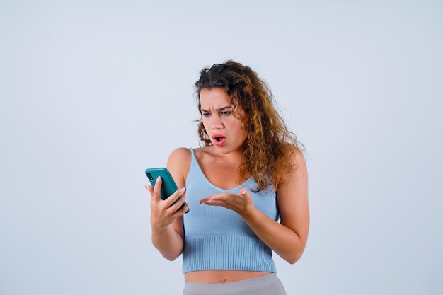 Une fille en colère regarde son écran mobile sur fond blanc