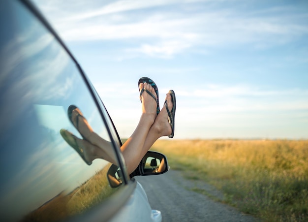 Fille collant ses pieds en tongs hors d'une fenêtre de voiture.