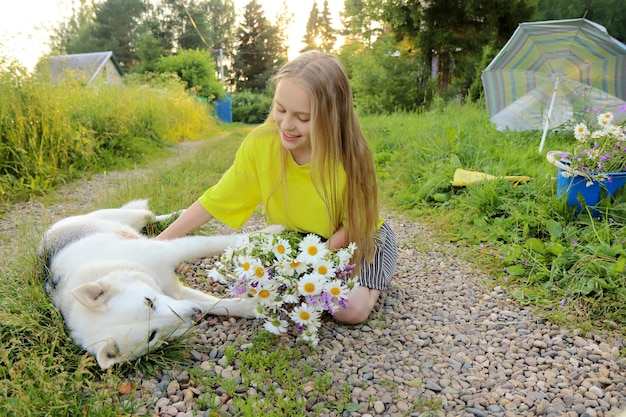 La fille communique en été avec son chien bien-aimé avec un bouquet de marguerites à la main.