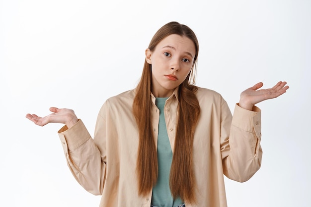 Une fille confuse et désemparée haussant les épaules ne peut pas dire ne sait pas n'a aucune idée debout sur fond blanc perplexe Copier l'espace