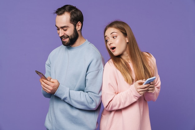 fille confuse regardant son homme discutant par téléphone portable isolé sur un mur violet.