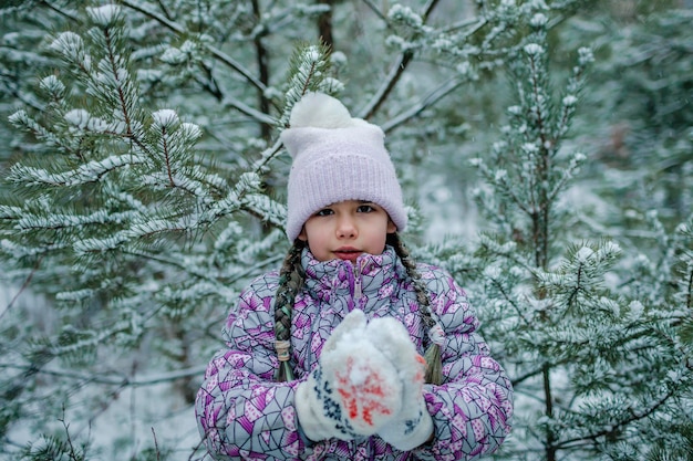Une fille congelée dans des vêtements chauds se promène en forêt avec le premier pays des merveilles d'hiver de neige tant attendu