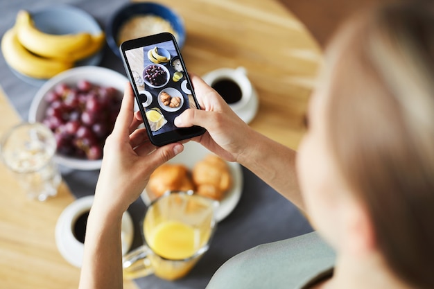 Fille contemporaine avec smartphone prenant une photo de sa table servie