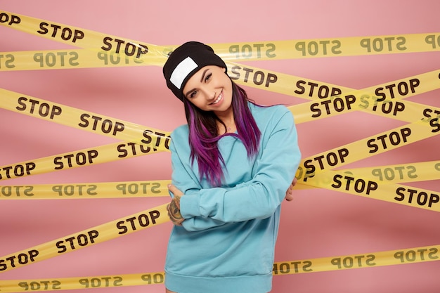 Une fille cool aux cheveux violets se dresse sur le fond d'un mur rose avec l'arrêt des bandes jaunes