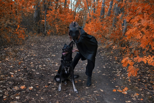 Une fille en costume bdsm et un masque noir et avec un chien dans la forêt rouge. une idée pour Halloween.