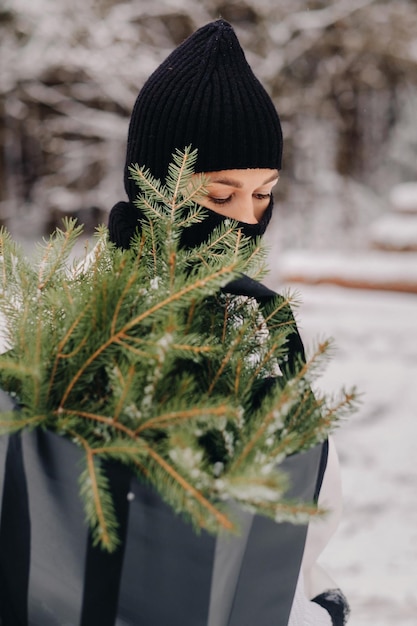 Une fille en costume blanc et cagoule avec un paquet d'arbres de Noël dans la forêt d'hiver le jour de l'an le concept du Nouvel An
