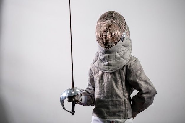 Une fille en costume d'escrime avec une épée à la main. Jeune modèle féminin pratiquant et exerçant. Sport, mode de vie sain.