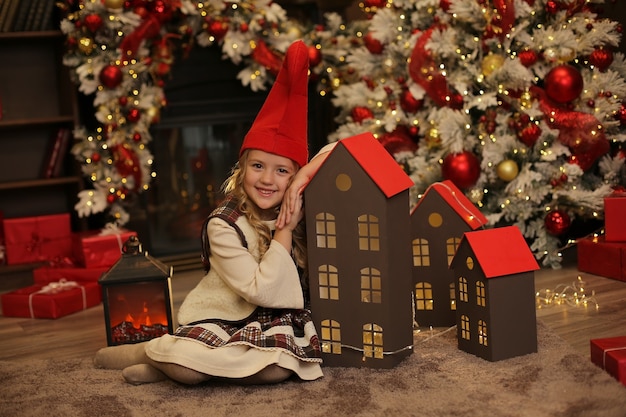 Une fille en costume de gnome s'appuya sur une maison en bois Atmosphère de Noël du Nouvel An