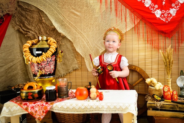 Une fille en costume national rouge près d'une table avec un samovar et des volants