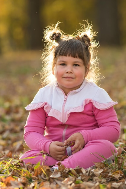 Une fille en costume rose assise sur le sol dans le parc d'automne