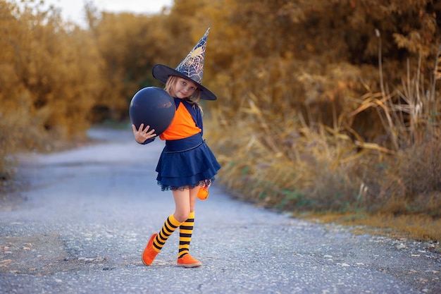 Une fille en costume de sorcière pour Halloween se promène dans la rue avec des chapeaux d'air festifs en forme de citrouilles Chapeau de sorcière
