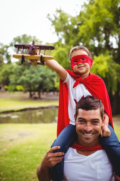 Fille en costume de super-héros assis sur les épaules du père