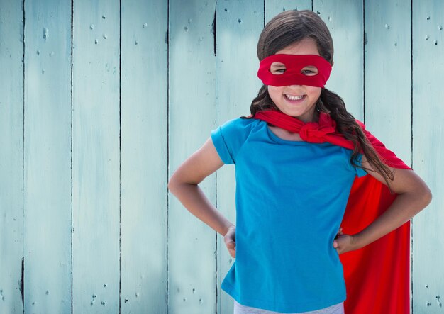 Fille en costume de super-héros avec les mains sur sa hanche debout contre un fond en bois