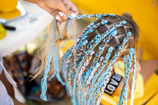 Une fille en costume tisse des tresses africaines dans ses cheveux par une journée ensoleillée