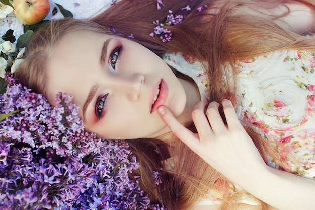 Fille couchée sur l&#39;herbe dans les branches de fleurs lilas