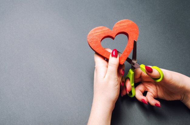 Fille coupe le coeur rouge avec des ciseaux. Le concept de rupture des relations, des querelles et du divorce.