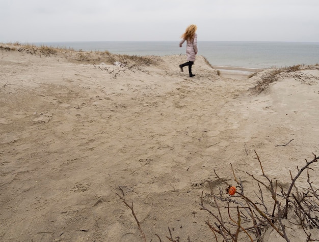 La fille court le long de la plage d'hiver sur l'isthme de Courlande par temps nuageux en Lituanie