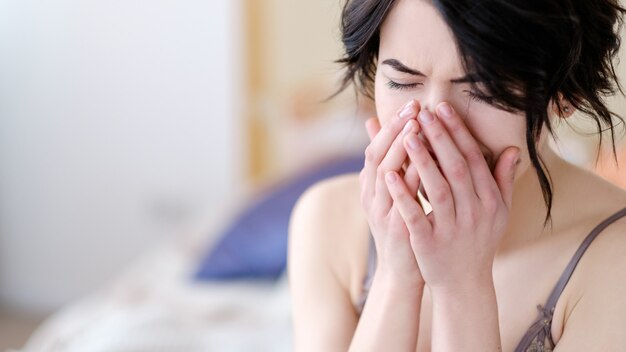 fille couvrant son visage avec les mains assis dans sa chambre en lingerie.