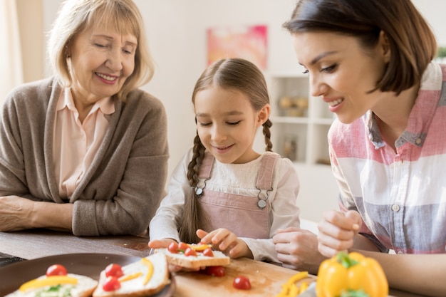 Fille créative faisant des sandwichs aux légumes pour le petit déjeuner entre sa mère et sa grand-mère