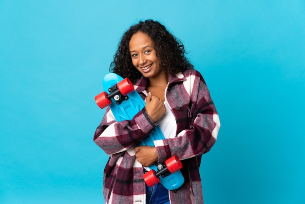 Fille cubaine adolescente isolée sur fond bleu avec un patin avec une expression heureuse