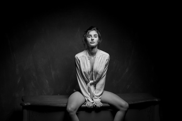 Une fille en culotte et une chemise blanche posant dans un intérieur vintage photo noir et blanc