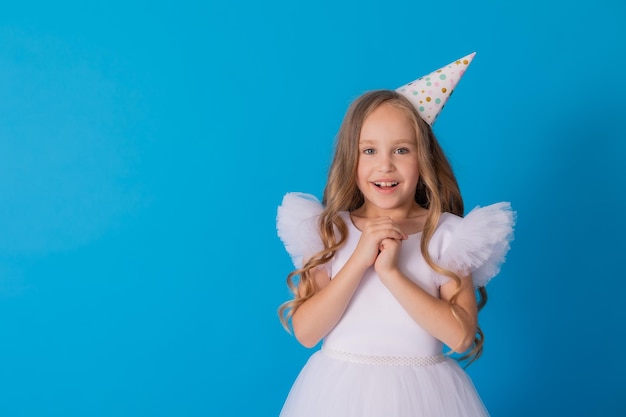 fille dans une belle robe et un chapeau en carton se dresse sur un fond bleu et jette des confettis