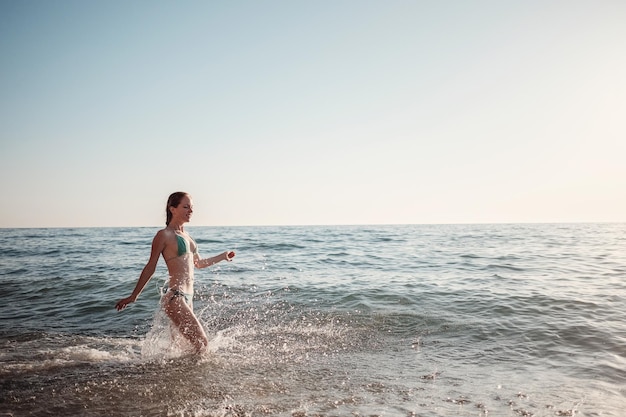 La fille dans un bikini court le long des vagues sur la plage en été