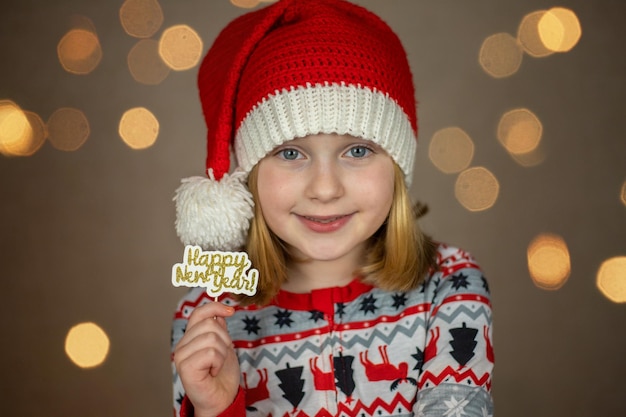 Une fille dans un bonnet de noel tient un signe de bonne année sur un fond de bokeh de nouvel an