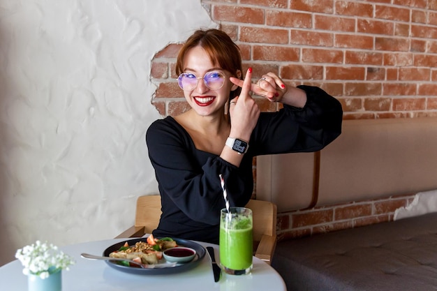 Une fille dans un café au petit-déjeuner montre divers gestes avec ses mains