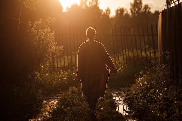 Une fille dans une cape marche le long d'un chemin au coucher du soleil