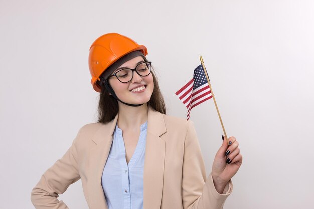 Une fille dans un casque de construction et un drapeau américain se tient heureux sur un fond blanc