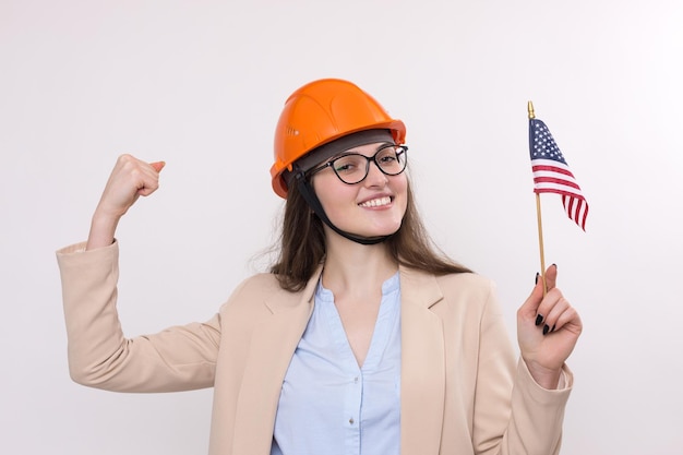 Une fille dans un casque de construction et un drapeau américain se tient heureux sur un fond blanc