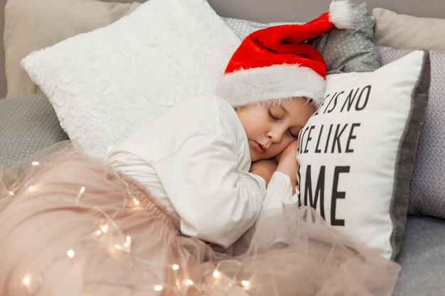 Une fille dans une casquette de Noël du Père Noël dort sur le lit