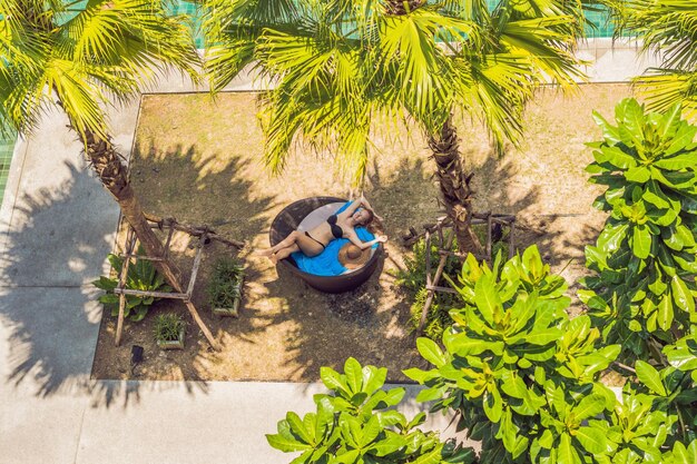 Fille dans des chaises longues parmi les palmiers près de la piscine.