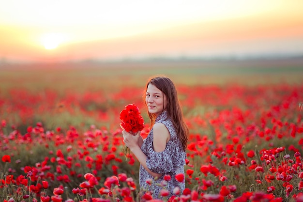 une fille dans un champ avec des coquelicots dans ses mains sourit